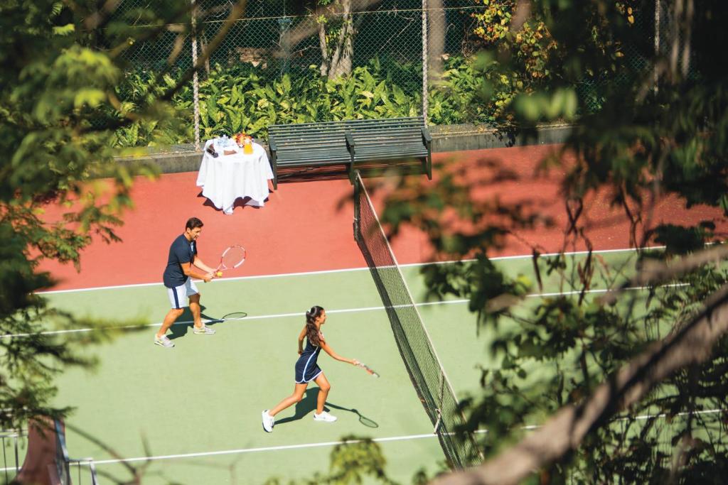 two people playing tennis on a tennis court at Reid's Palace, A Belmond Hotel, Madeira in Funchal