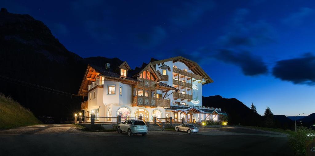 a large building with two cars parked in front of it at Hotel Cristallo in Passo San Pellegrino