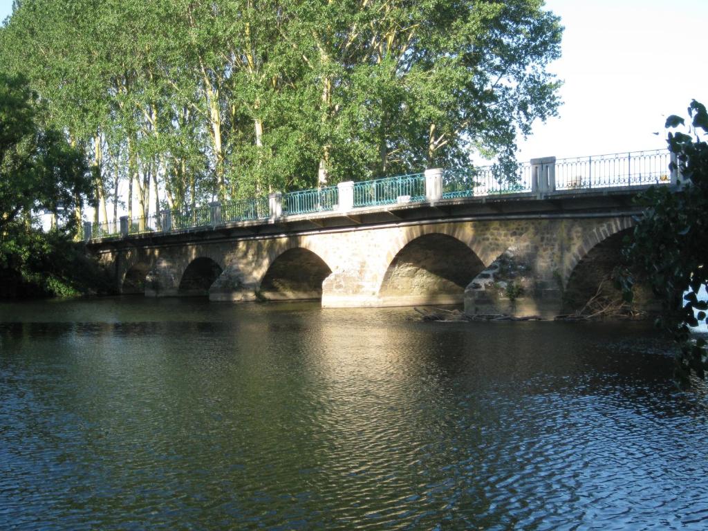 un puente sobre un cuerpo de agua con árboles en Le Petitepinay, en Moitron-sur-Sarthe