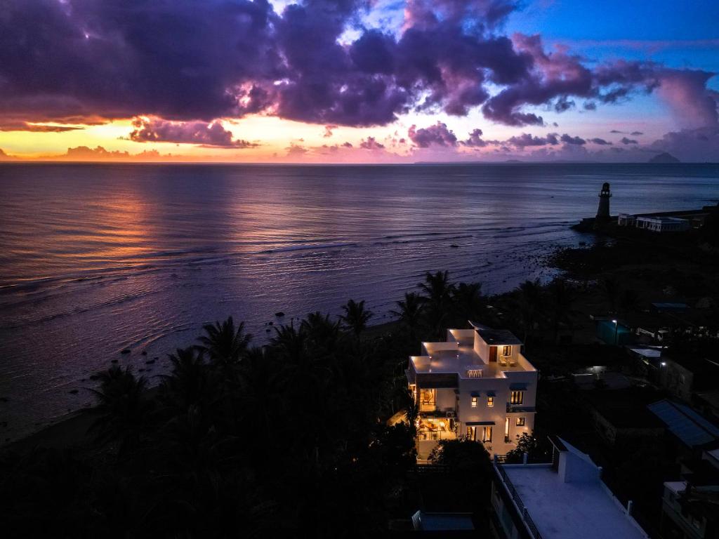 zachód słońca nad oceanem z domem i latarnią morską w obiekcie Villa Ferrer w mieście Mahatao