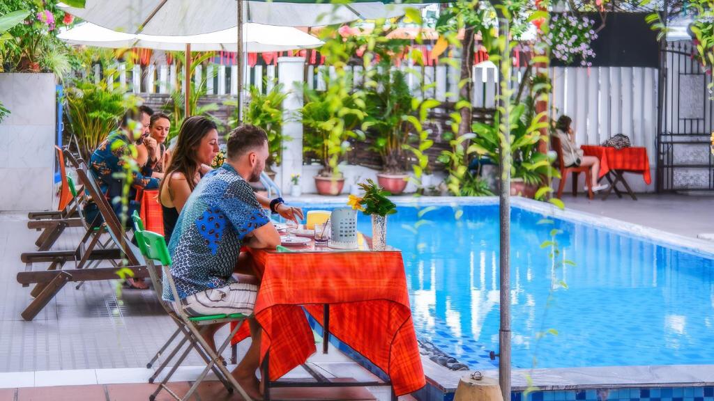 a man and woman sitting at a table by a pool at Oleander Garden Homestay in Hoi An