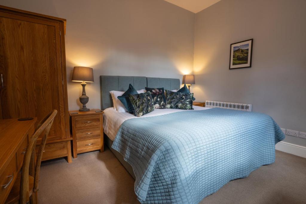 a bedroom with a bed with a blue blanket and a desk at Hassop Station rooms on the Monsal Trail in Bakewell
