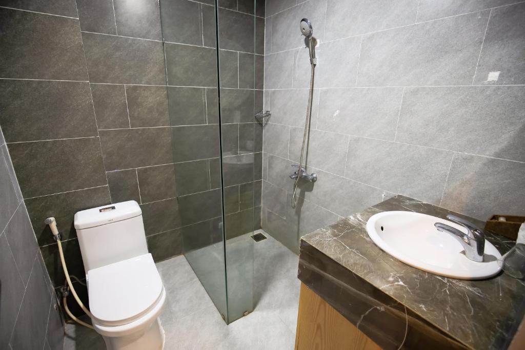A compact gray-tiled bathroom with a glass shower partition, toilet, and marble-look vanity.