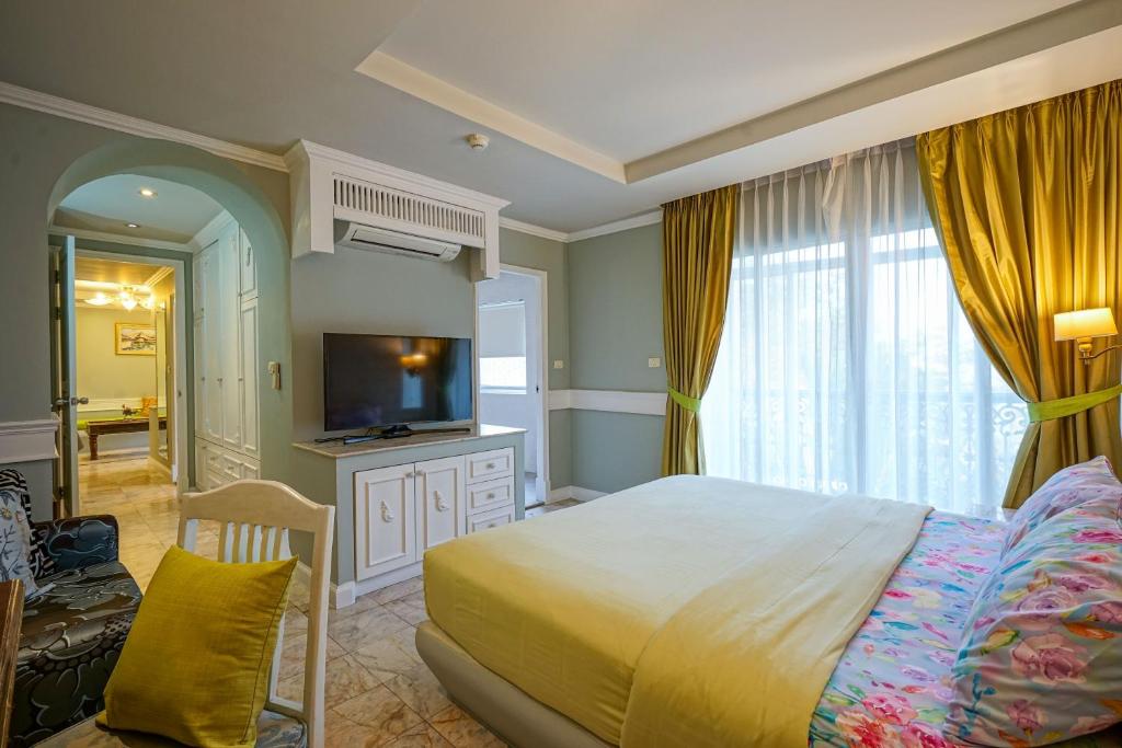 A bedroom with a large bed, television cabinet, armchair and curtained window.