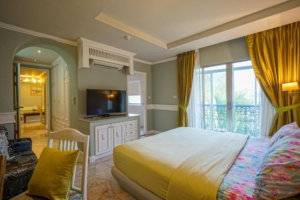 A large bedroom with a television, lounge chair, and curtained balcony or window opening.