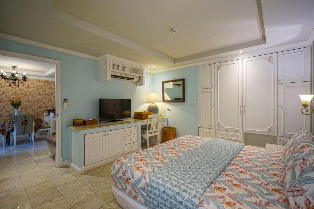 A bedroom with a television, desk, extensive wardrobes and a glimpse of the dining kitchen.