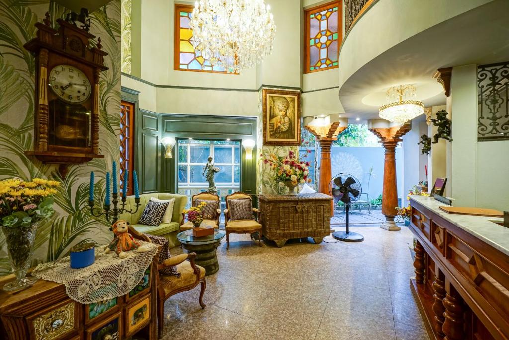 A spacious ornate lobby lounge with a grandfather clock, seating, chandeliers and an open entrance area.