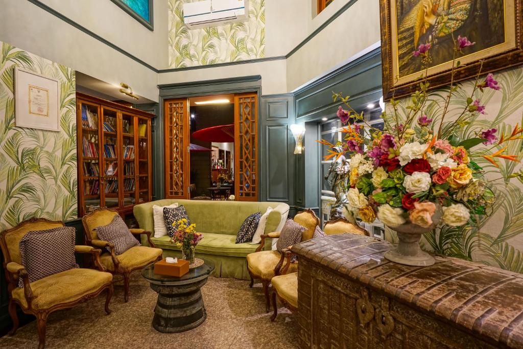 A richly decorated lobby lounge with a green sofa, armchairs, chandelier and oversized flower arrangement.