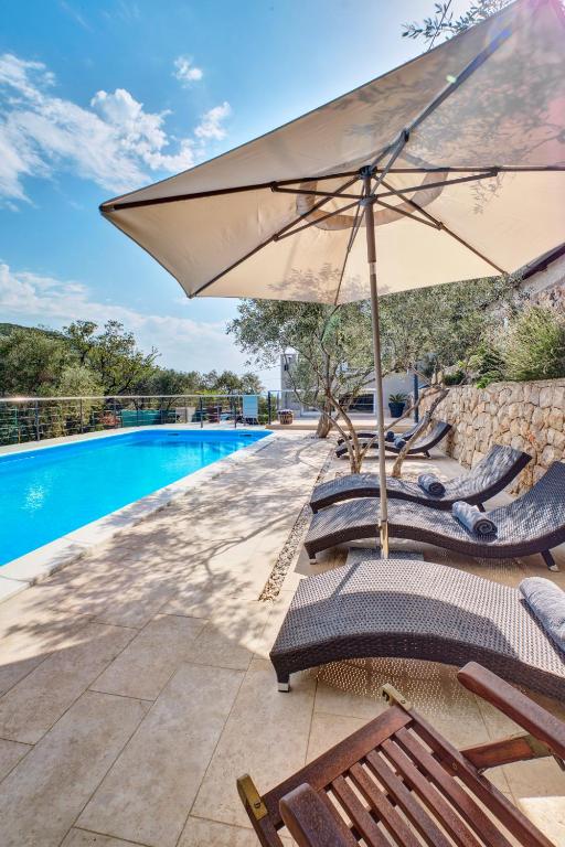 an umbrella and lounge chairs next to a swimming pool at Apartments Alberta in Miholašćica