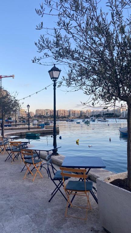 a group of tables and chairs next to a body of water at Malta Crown guesthouse in St. Julianʼs
