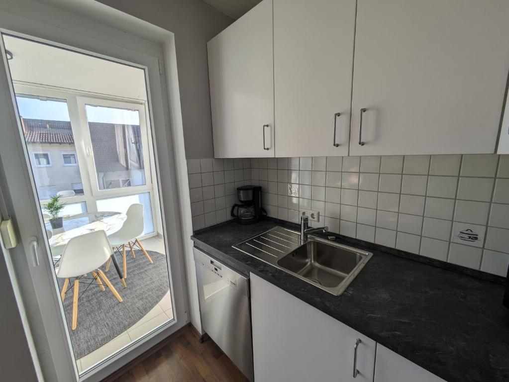 cocina con armarios blancos, fregadero y ventana en FeWo Lorenz, en Buchen