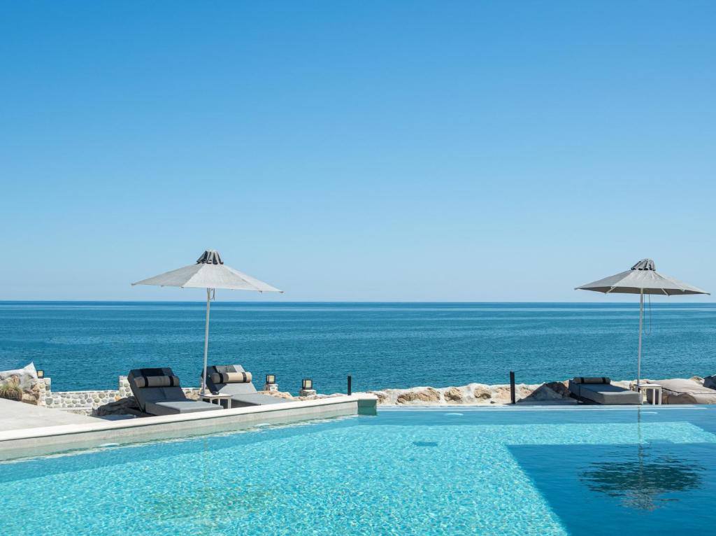 una piscina con sedie, ombrelloni e oceano di Akrotiri Olympus Luxury Suites - Adults Only a Plaka Litochorou