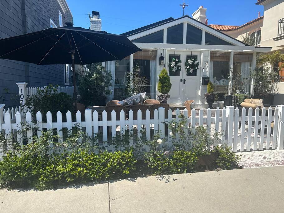 a white fence in front of a house with an umbrella at Balboa Island Beach Cottage with Golf Cart in Newport Beach