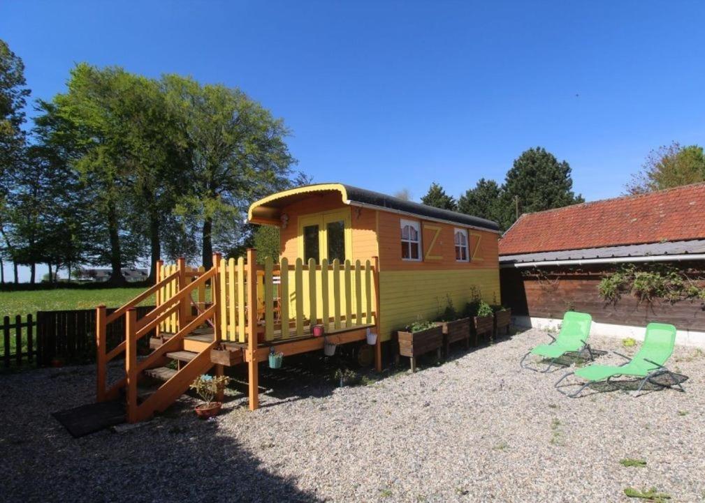 een klein geel huis met een glijbaan en twee stoelen bij La roulotte du bois du fil in Vassonville