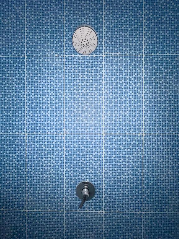 una ducha de azulejos azules con reloj en la pared en TANAWU AIRPORT HOTEL LOMBOK en Praya