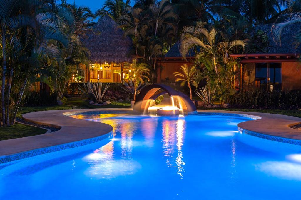 una piscina con luces azules en un patio trasero por la noche en The Inn Manzanillo Bay, en Troncones