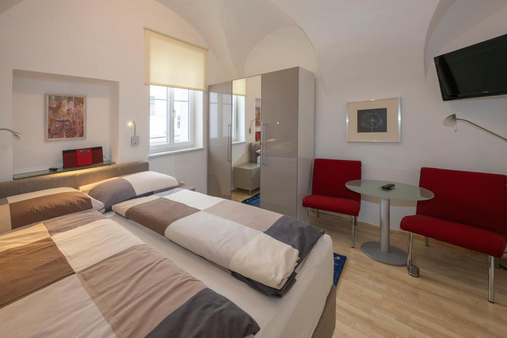 クラーゲンフルトにあるApartments Alter Platzのベッドルーム1室(ベッド2台、テーブル、赤い椅子付)