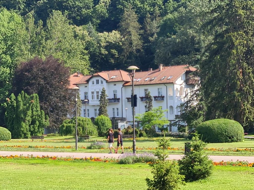 two people walking in front of a large white house at Slatkiš Sweet in Banja Koviljača