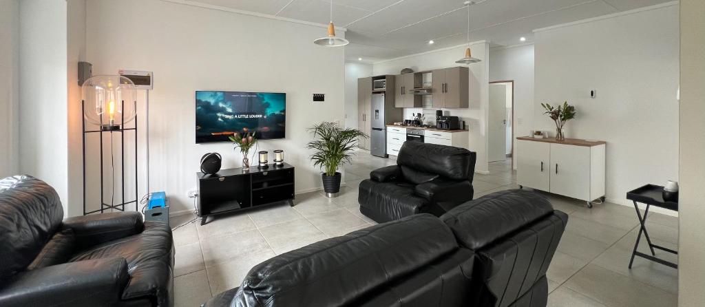 a living room with black leather couches and a kitchen at Boschkloof Bliss in George