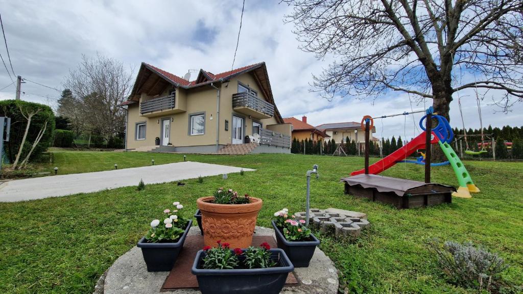 uma casa com um parque infantil e algumas plantas num quintal em Silence Apartmanház Zalakaros em Zalakaros