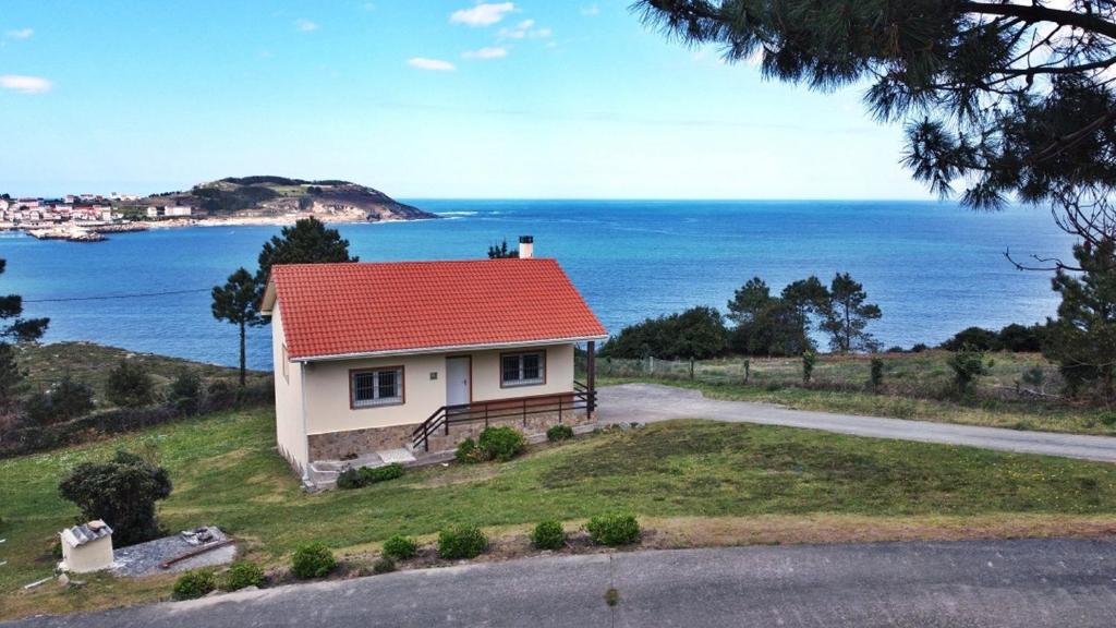 een huis met een rood dak op een heuvel naast de oceaan bij Casa en primera linea de mar. in Laxe