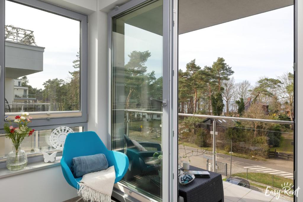 Habitación con ventanas grandes y silla azul. en Grunwaldzka 12 C22 Easy - Rent Apartments - 50m od plaży en Pobierowo