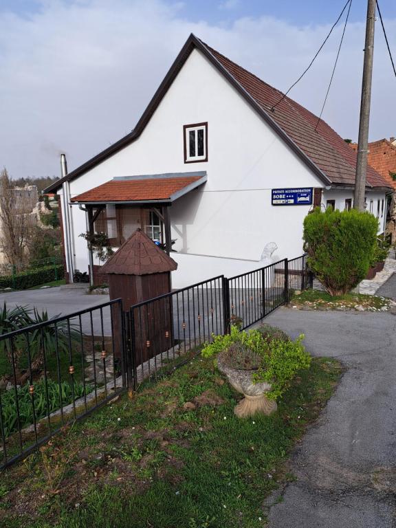 a white house with a fence in front of it at Rooms Modrušan in Slunj