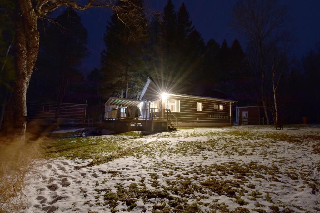 a cabin in the snow at night with a light at Alison A Romantic Getaway With Private Hot Tub in Rivière-Rouge