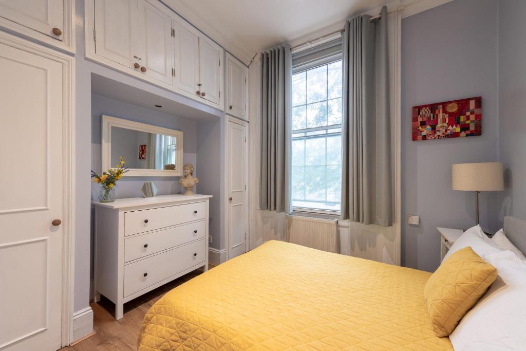 a bedroom with a yellow bed with a dresser and a window at Stunning Bright flat in London