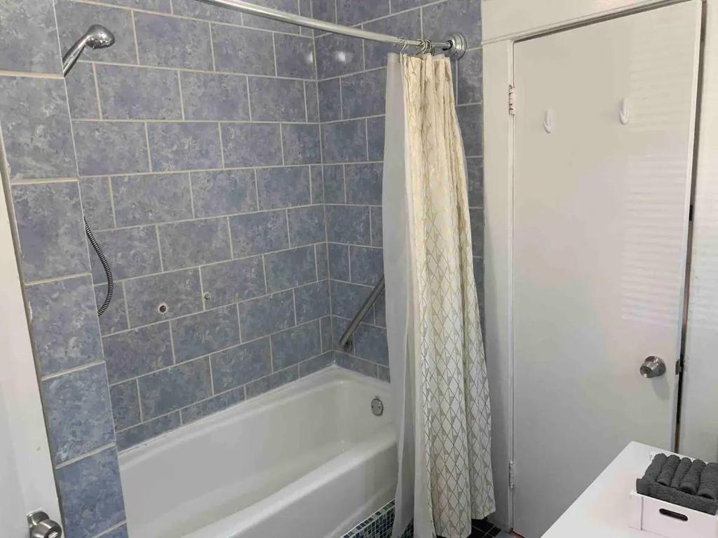 baño con bañera blanca y azulejos azules en Cozy 1-bedroom in a Brazilian home, en Los Ángeles