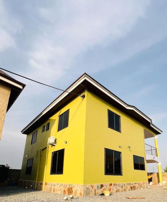 una casa amarilla con techo negro en Serene Getaway: 5-bedroom Duplex, en Dawhwenya