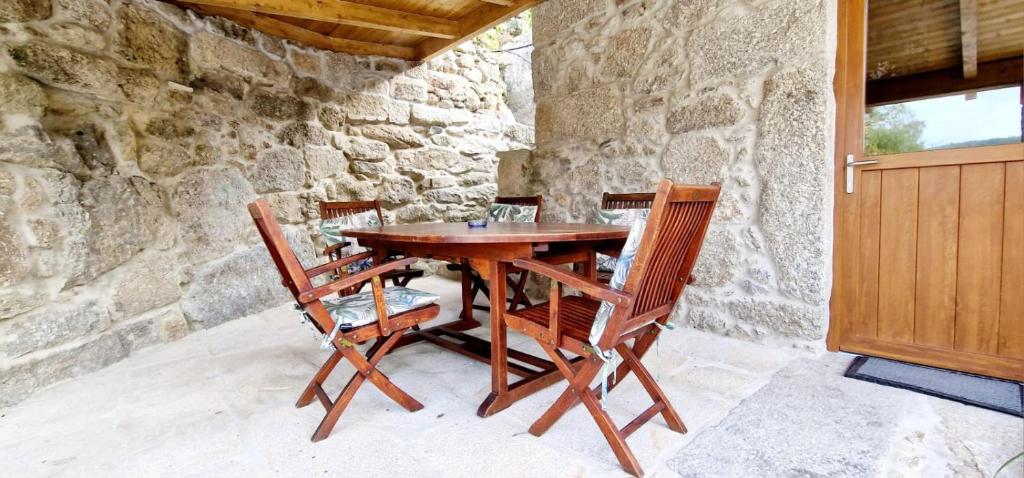 a wooden table with four chairs and a stone wall at Quinta de Sito in Chantada
