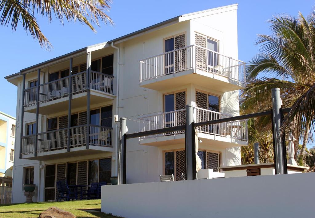 a white building with balconies and palm trees at Bargara Shoreline Apartments in Bargara