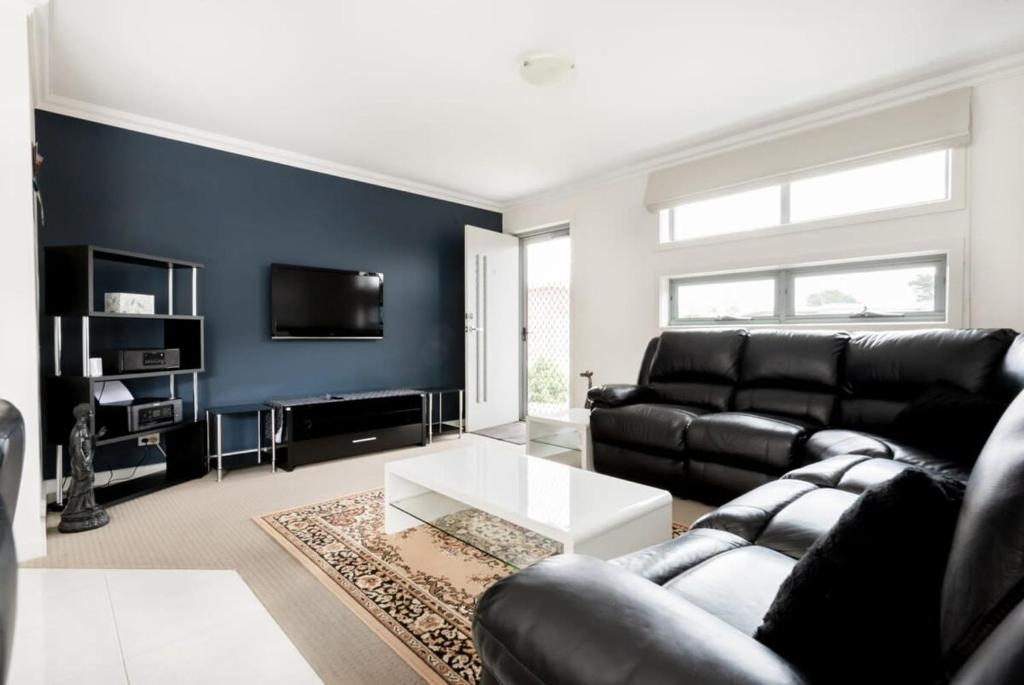 een woonkamer met een zwarte leren bank en een tv bij Comfortable Home 10 Minutes from Town - Wifi and Garage in Newnham