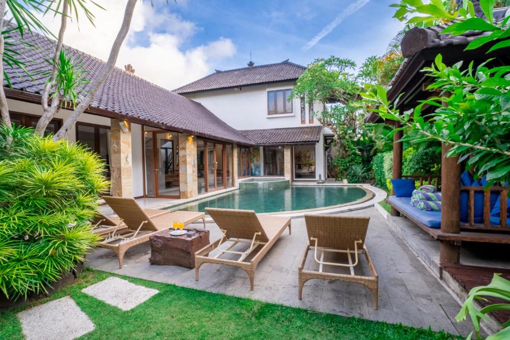 a backyard with a pool and chairs and a house at Enclose living 5Br Villa Center of Seminyak Near Beach in Seminyak