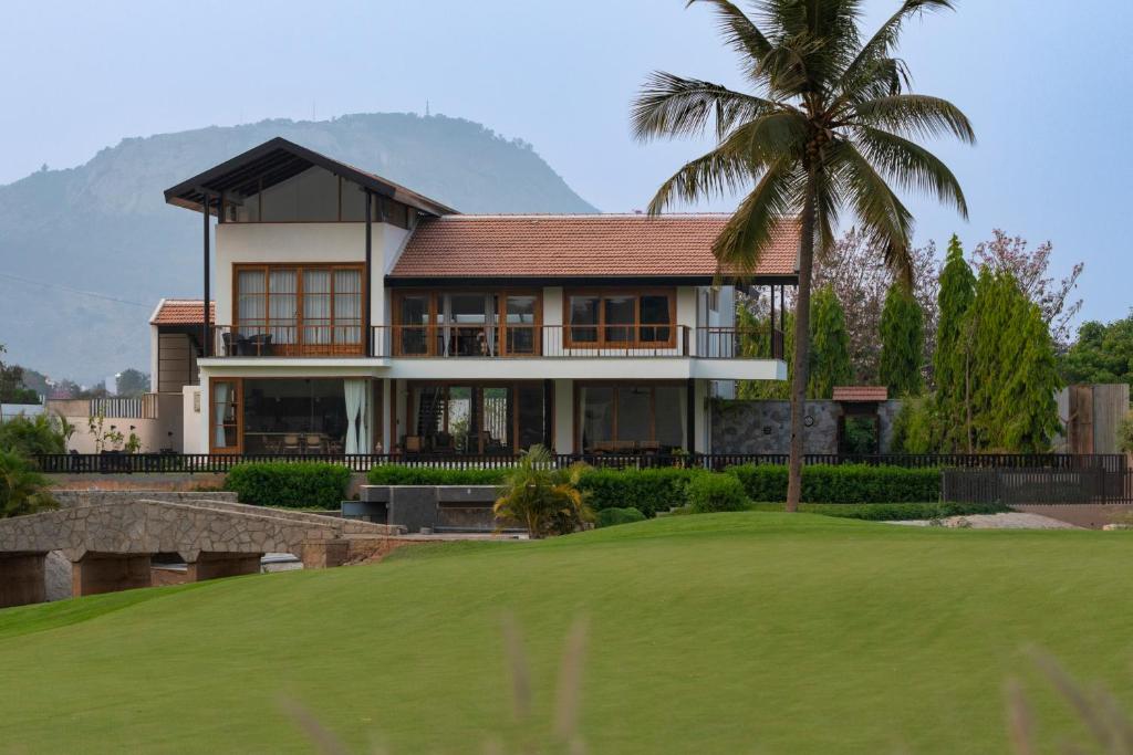 a house with a palm tree in front of a green at SaffronStays Niranta- Villa in Golfshire, Nandi Hills in Bangalore