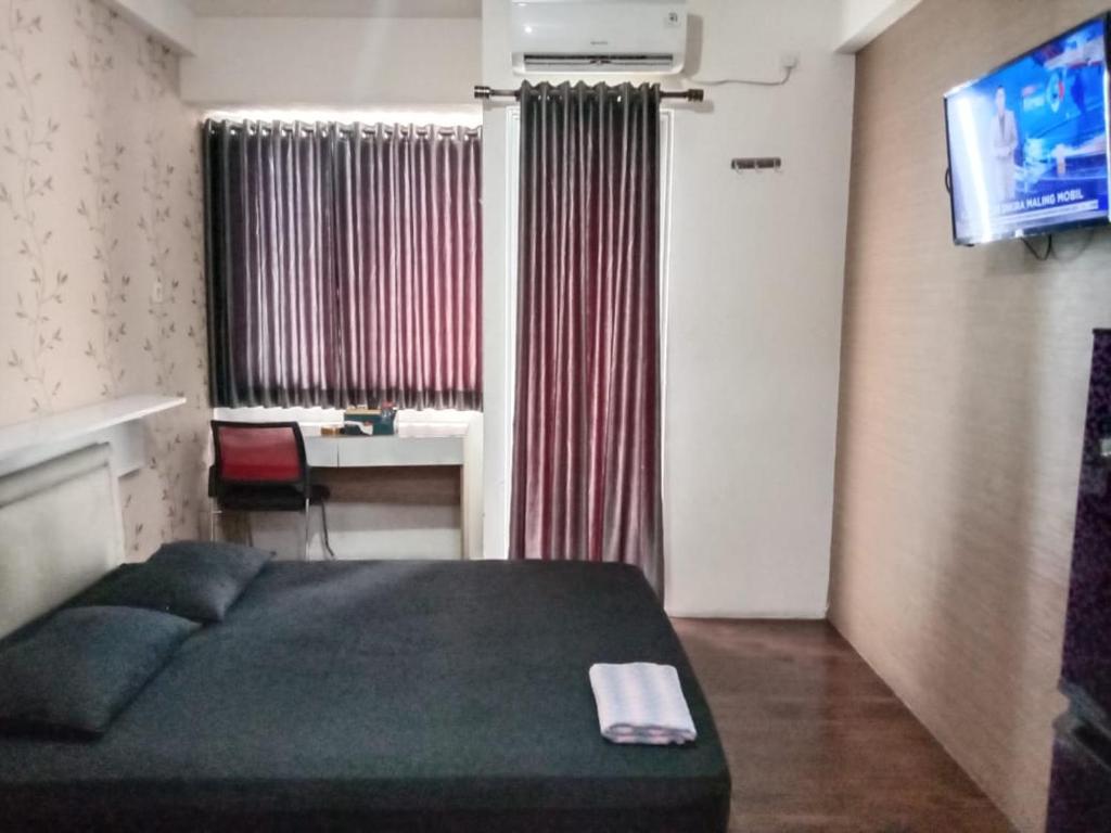 een slaapkamer met een bed, een bureau en een televisie bij Apartemen Riverview Sewa Room in Tegalgede