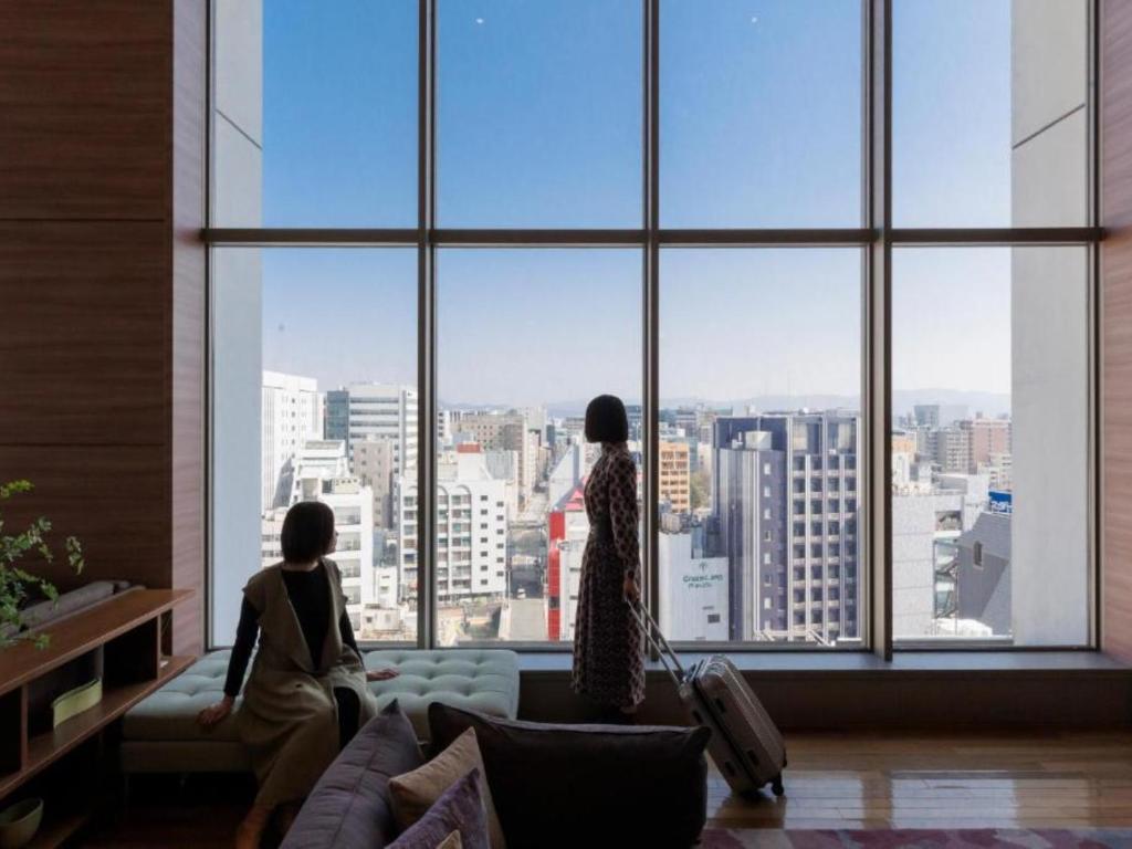 zwei Frauen, die aus einem großen Fenster in eine Stadt blicken in der Unterkunft Hotel Resol Trinity Hakata in Fukuoka