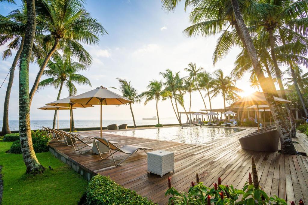een houten terras met een zwembad en palmbomen bij Nirwana Beach & Resort in Candidasa