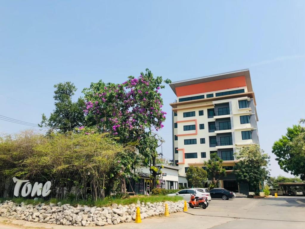 um edifício com uma árvore com flores cor-de-rosa em frente em Tone Condorent Hotel em Chachoengsao