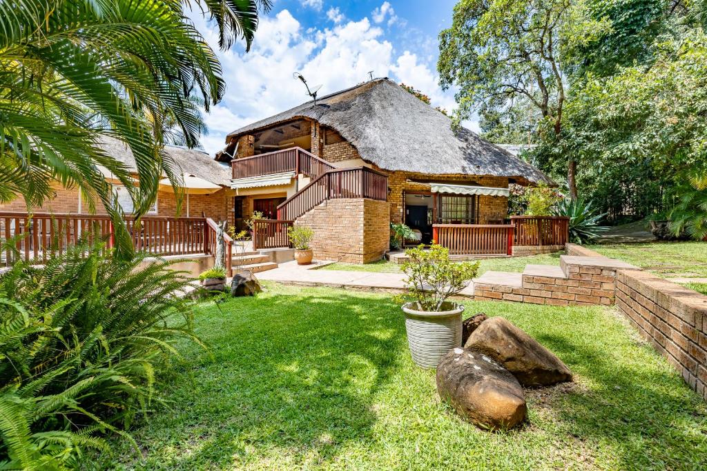 a brick house with a thatched roof in a yard at Woodlands Guest House in Hazyview