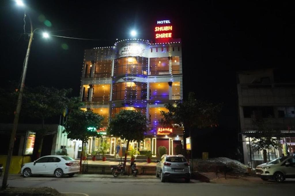 oświetlony budynek w nocy z samochodami zaparkowanymi przed budynkiem w obiekcie Hotel Shubh Shree Bilaspur w mieście Bilaspur