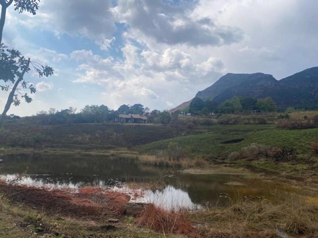 un campo con un estanque en un campo con montañas en Chalet 20, Fernwood Estate, Drakensberg, en Mountain Herberg Hostel