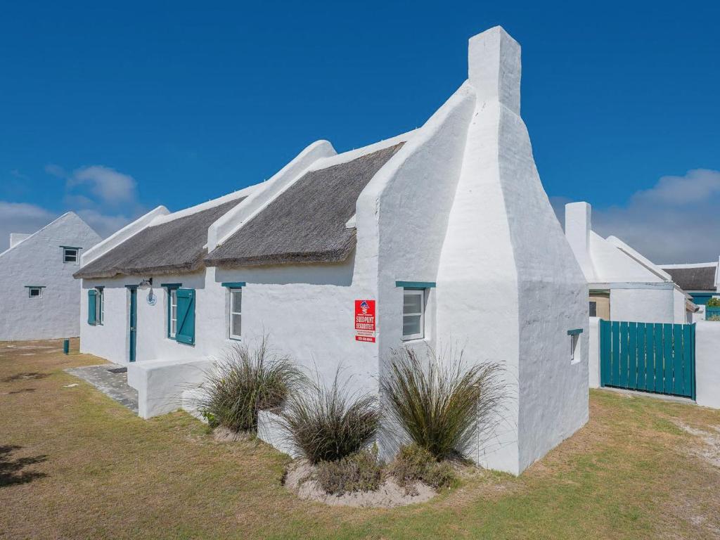 una casa blanca con techo gris y plantas en Zandtorini Seaside Cottage, en Struisbaai