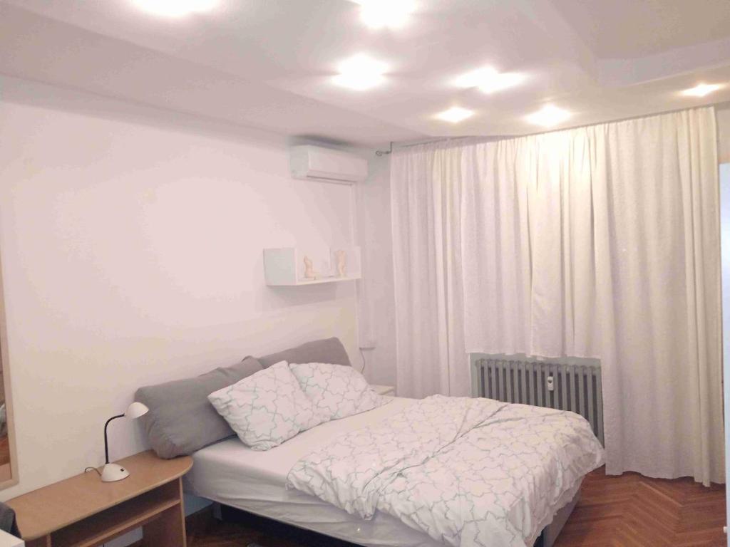 a white bedroom with a bed and a table at Apartman Selska in Zagreb