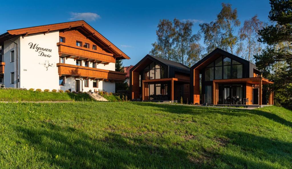 a house on a grassy hill next to a building at Wysowa Dwór Domki in Wysowa-Zdrój