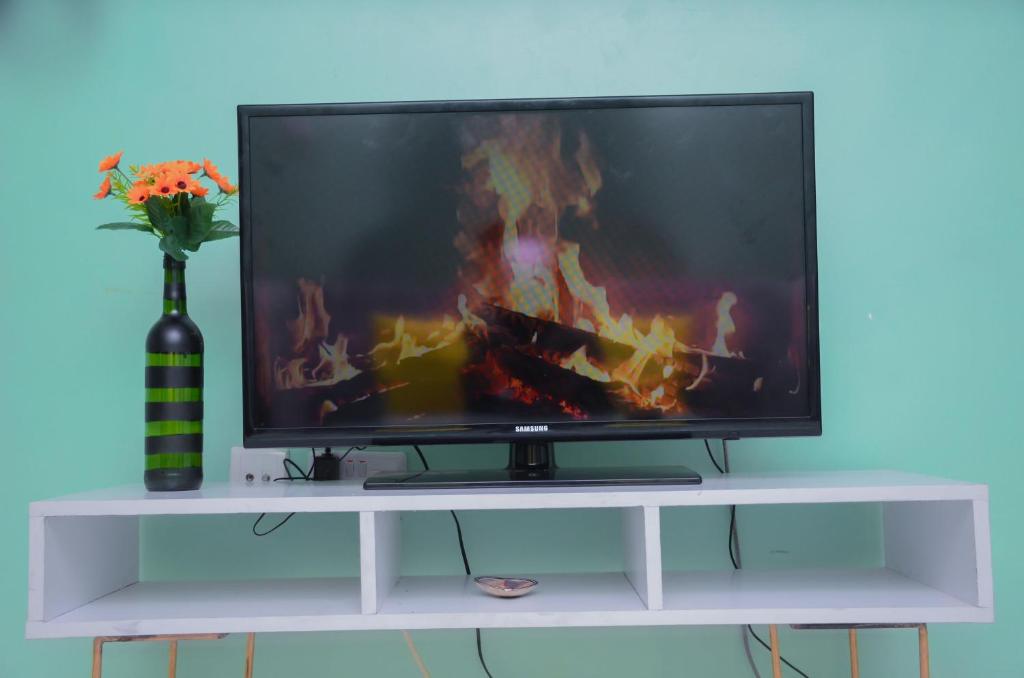 a television on a white stand with a vase of flowers at Amani Homes in Eldoret