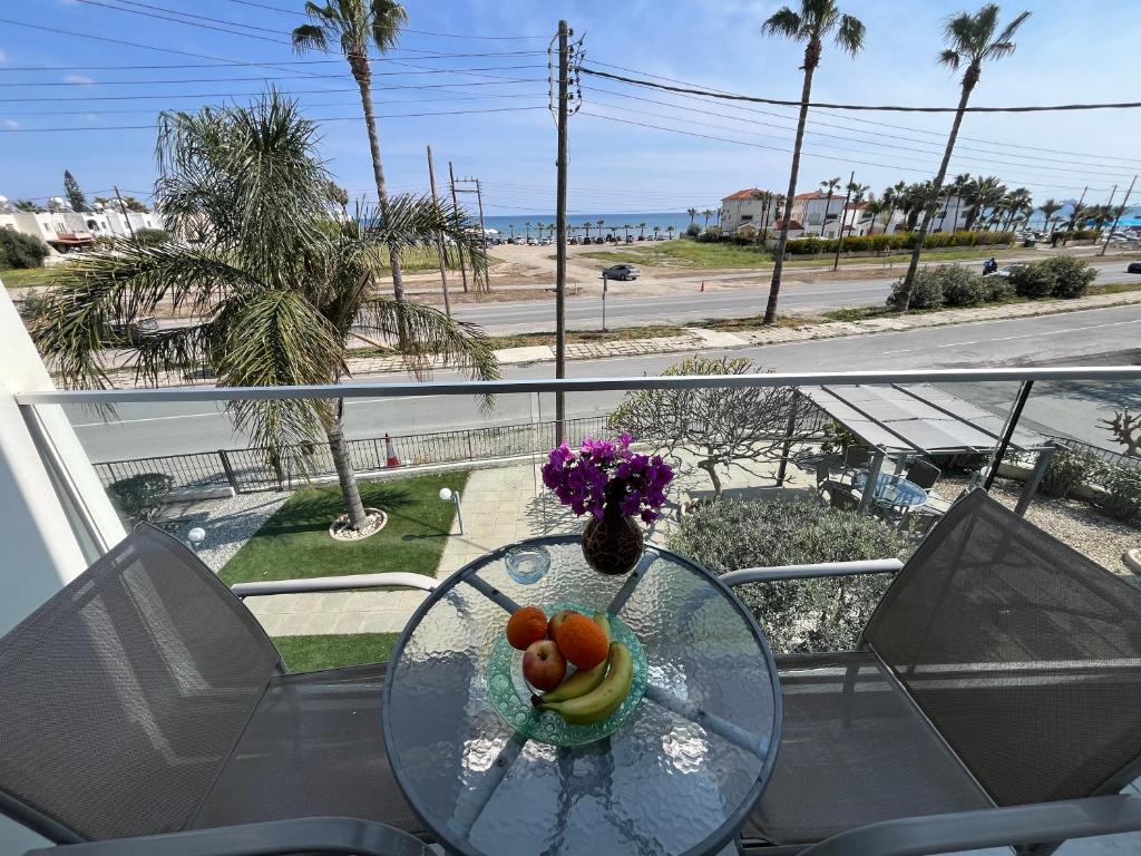 a glass table with a bowl of fruit and flowers on a balcony at Themis Apartments in Larnaca