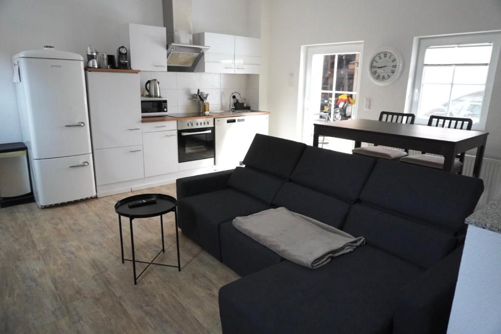 ein Wohnzimmer mit einem schwarzen Sofa und einer Küche in der Unterkunft BayrischGut Ferienwohnung in Orschweier