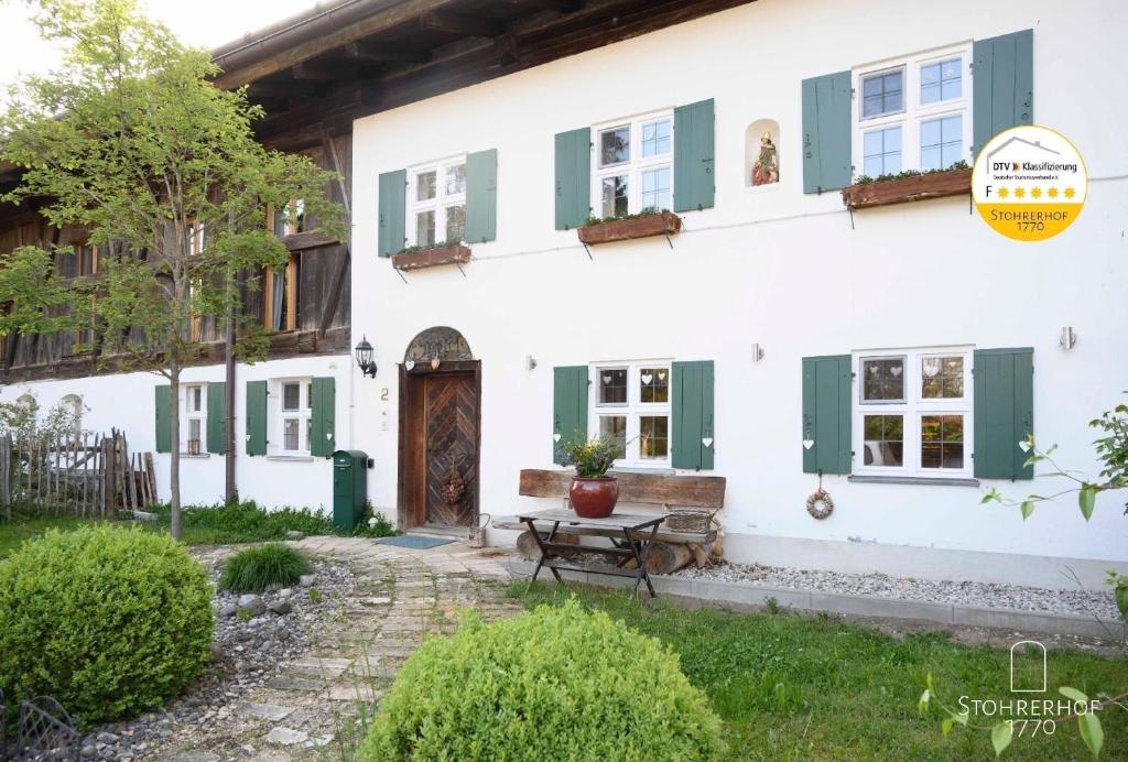 ein weißes Haus mit grünen Rollläden und einer Bank in der Unterkunft Wunderschönes Ferienhaus in Riederau mit Offenem Kamin in Dießen am Ammersee